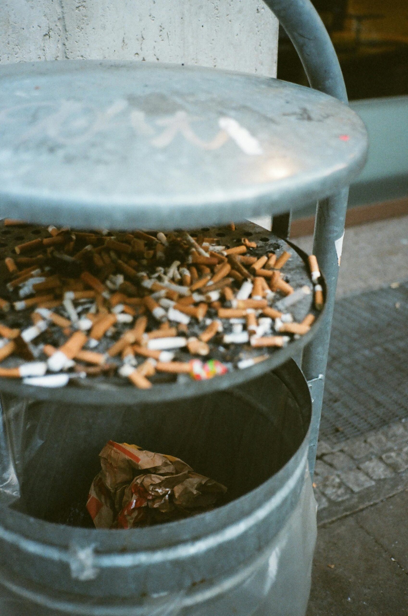 Image of a crowded ashtray filled with cigarette butts atop a trash bin. Urban waste scene.
